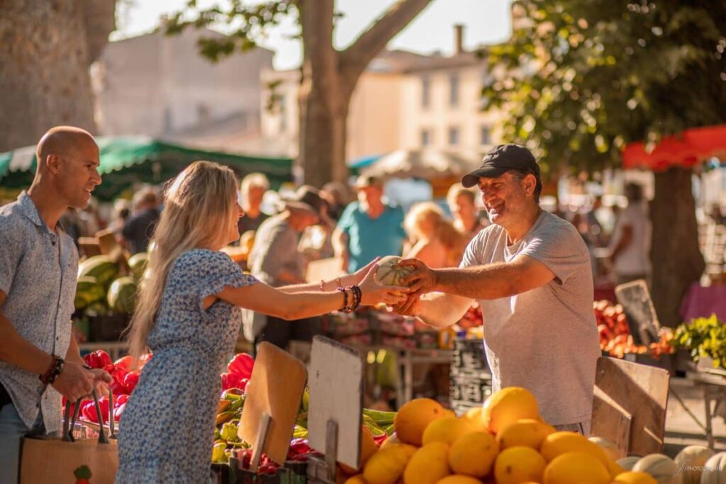 Un marché provençal avec des artisans en action. Un vendeur d'hommes sur un marché aux légumes et fruits remet un melon à un couple