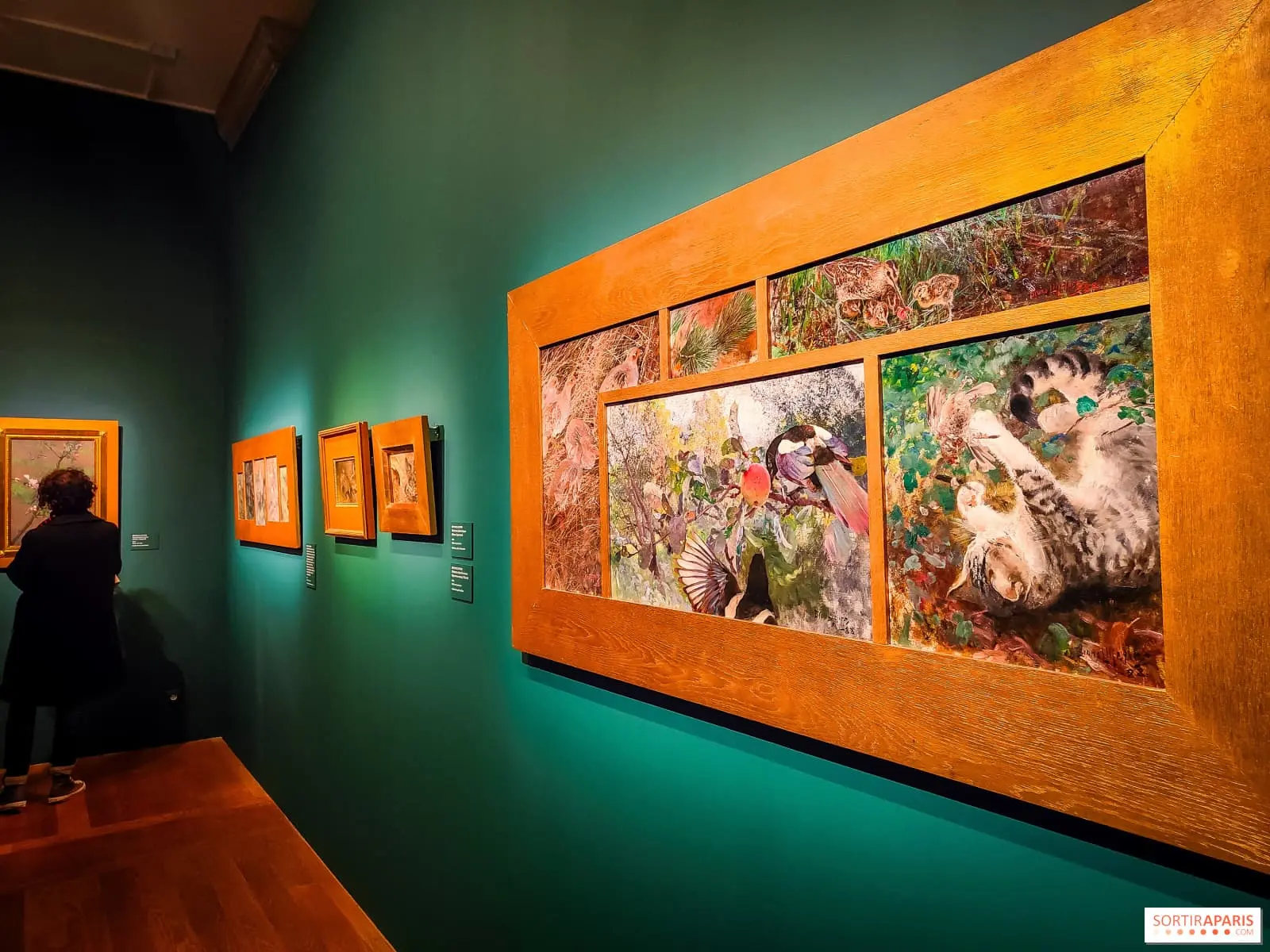 Mur de musée avec plusieurs tableaux accrochés.